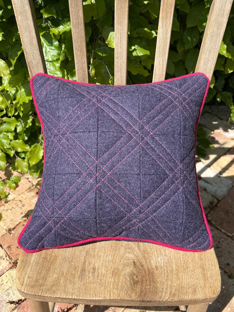 Quilted purple wool cushion with contrasting pink piping, perfect for adding a touch of elegance to any space.