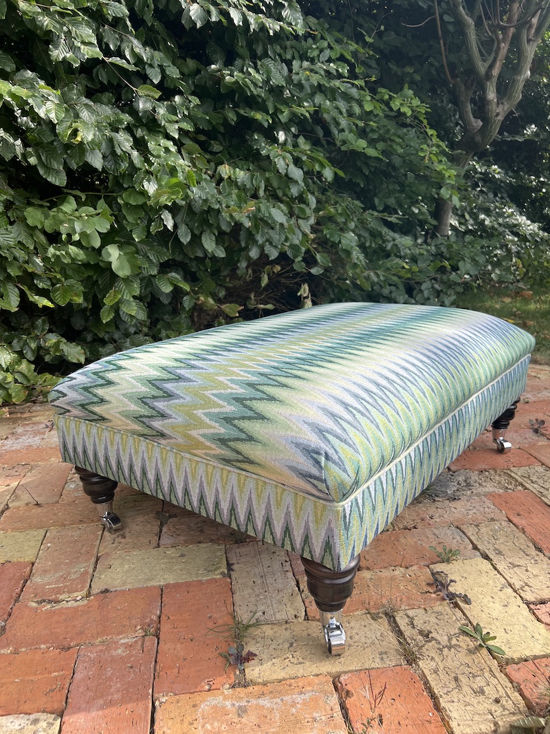 Elevate your space with the SEA SPRAY FOOTSTOOL, featuring vibrant zigzag upholstery and classic wooden legs on casters.