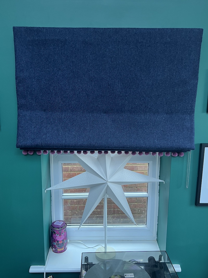 Wool Roman blind in deep blue with playful pom-pom trim, elegantly enhancing any window space.